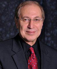Portraid of Dr. Mazen E. Hamad wearing a black suit and a red tie against a black backdrop