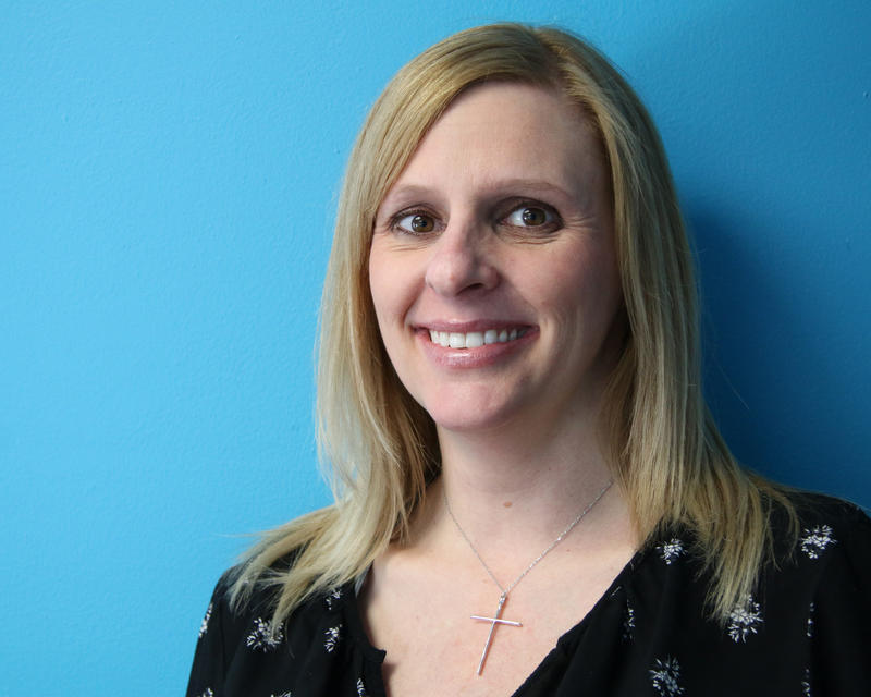 she has long blonde hair, wears a black blouse and a cross