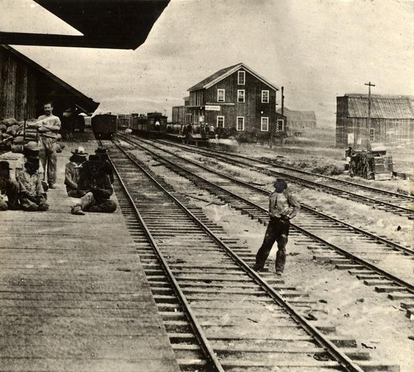 A black and white image of Reno's original railroad depot in 1868, where some figures stand by three sets of tracks.