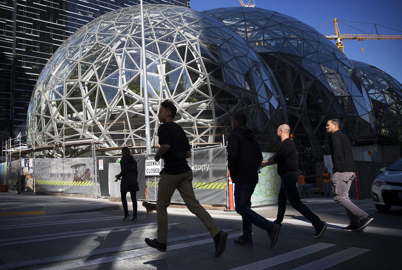 A group of people jog across Lenora Street, on Thursday, October 5, 2017, in front of Amazon's biodomes, in Seattle.