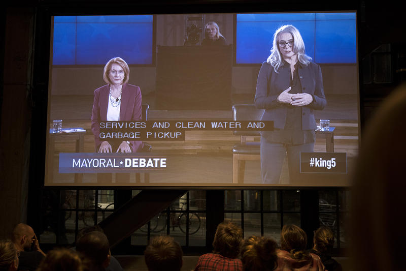 Mayoral candidates Jenny Durkan, left, and Cary Moon are shown on a screen during a mayoral debate viewing party on Tuesday, October 24, 2017, at Optimism Brewing Company in Seattle.