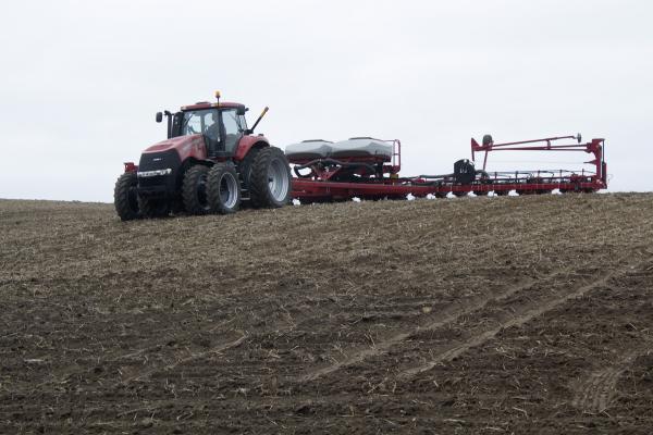 A farm hand on the Nelson farm in north Iowa drives a tractor pulling a 24-row planter as it drops corn seeds into the field. 
