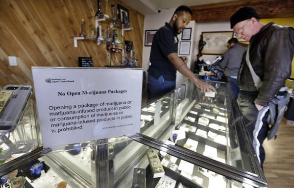<p>Cannabis City clerk Will Bibbs, left, helps a customer looking over a display case of marijuana products at the shop in Seattle.</p>