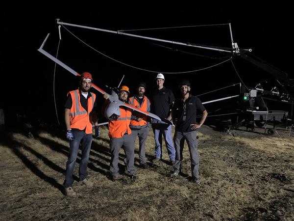 Insitu unmanned aircraft operators pose with the ScanEagle drone after disconnecting it from the "SkyHook" retrieval system behind them.