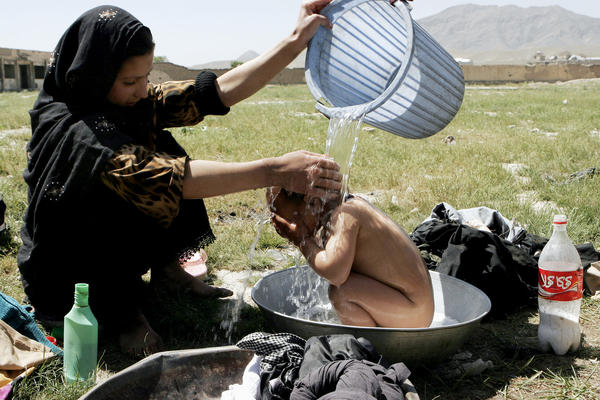 An Afghan girl bathes her brother near a building where refugees live in Kabul, 2007.