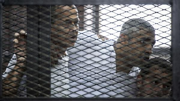 Australian journalist Peter Greste (left) of Al-Jazeera news channel and his colleagues, Egyptian-Canadian Mohamed Fadel Fahmy (center) and Egyptian Baher Mohamed, listen to the verdict inside the defendants' cage during their trial for allegedly supporting the Muslim Brotherhood.