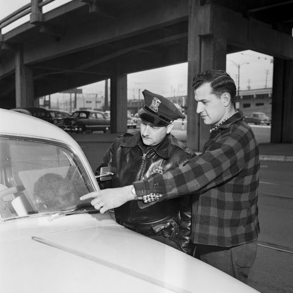 A man shows his pitted windshield to a police officer in Seattle in 1954