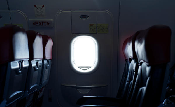 Where should you sit on a plane to reduce the risk of exposure to germs spread by infectious passengers?