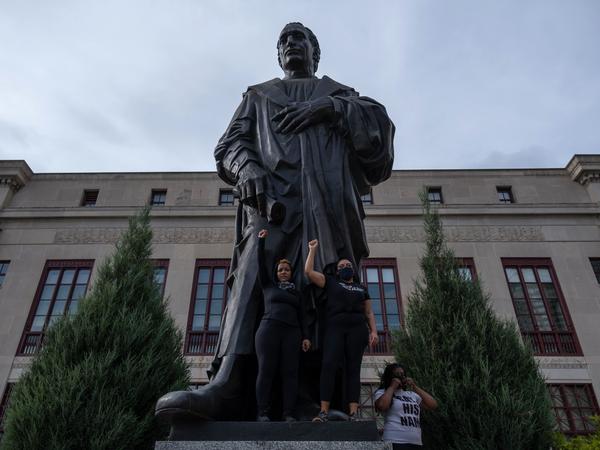Demonstrators stand on the base of a Christopher Columbus statue in front of City Hall during a protest against police brutality Saturday in downtown Columbus, Ohio.