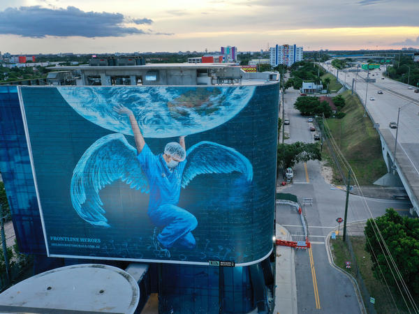 A billboard in Miami — where coronavirus cases continue to surge — depicts a medical worker holding up the world. The number of coronavirus deaths worldwide has surpassed 600,000, with more than 140,000 of those in the U.S.