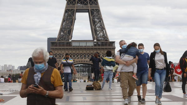 People wearing masks walk near the Eiffel Tower in Paris on Thursday, the same day that the government made masks mandatory in all the city's public outdoor spaces.