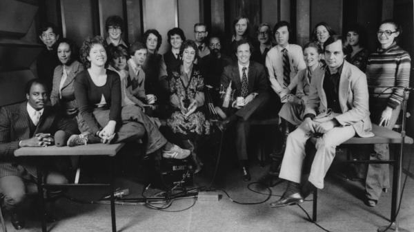 A staff photo taken during the early days of <em>Morning Edition. </em>Co-host Bob Edwards is in the back row, standing seventh from the left among the three men in glasses. His co-host, Barbara Hoctor, sits on the table at right, holding a mug. Hoctor left the show after a few weeks. Edwards was host until 2004, when he went to SiriusXM.
