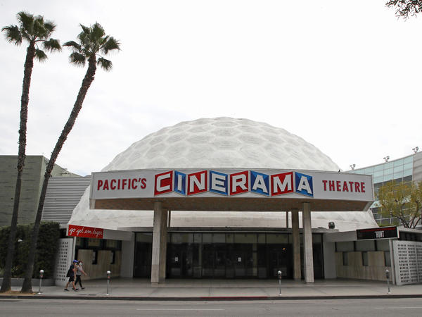People wearing protective face masks walk by the closed Cinerama Dome theater during the coronavirus pandemic on April 18, 2020, in Los Angeles.