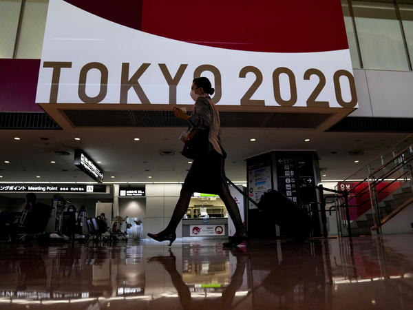 A flight attendant walks by a large display of Tokyo 2020 Olympics at Narita International Airport on Thursday in Narita, east of Tokyo.
