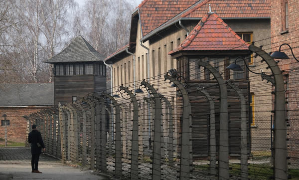 A visitor walks near barbed wire and prison barracks at the former Auschwitz I concentration camp on Jan. 26, 2020, in Oswiecim, Poland.