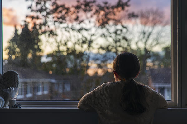 A girl looks out of her bedroom window as the sun is setting.