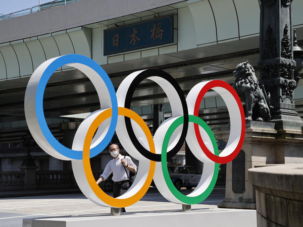 A man wearing a face mask walks past the Olympic Rings ahead of the Tokyo 2020 Olympic Games. The Games are scheduled to begin this week in Japan despite a global rise in coronavirus cases.