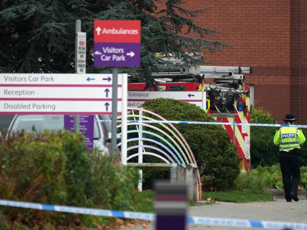 A police officer walks past a fire engine at Liverpool Women's Hospital in Liverpool, England, on Monday. One person died and another was injured after a device exploded in a taxi outside the hospital on Sunday.