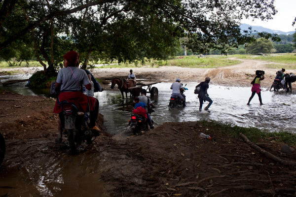 Colombian guides and migrants walk and ride motorcycles at the beginning of the journey through the Darién Gap. To cover the first few miles, migrants can pay to ride on the back of motorcycles that navigate muddy trails. But soon the jungle thickens, and they must start walking.