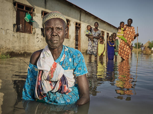 Nyayua Thang, 62, left, stands waist-deep in the floodwaters in front of an abandoned primary school in South Sudan. Members of her village, displaced by extreme flooding as a result of heavy rainfall, are using the building as a refuge. Only small mud dikes at the entrance of the door are keeping the water out. (November 2020)