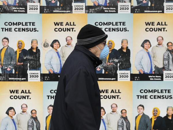 A person wearing a mask walks past posters encouraging census participation in Seattle in April 2020. The coronavirus pandemic has disrupted not only last year's national head count, but also a critical follow-up survey that the U.S. Census Bureau relies on to determine the tally's accuracy.