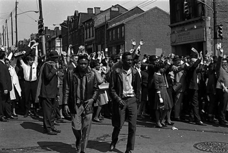 Several people stand with raised hands as the crowd gathers at the corner of Crawford Street and Centre Avenue near Mendelsohn's Ice Cream Bar for the march from the Hill District to Downtown and the Point scheduled three days after the assassination of Dr. Martin Luther King Jr. (Charles R. Martin Photographs/University of Pittsburgh)