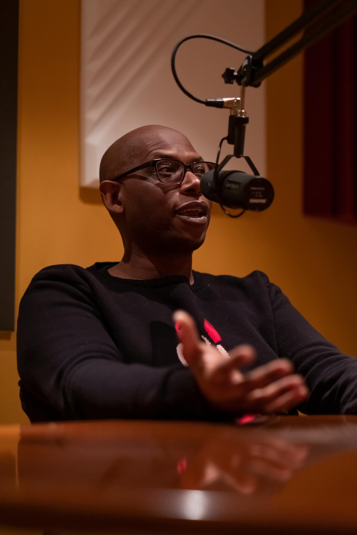 a man in a black shirt with glasses speaking into a microphone